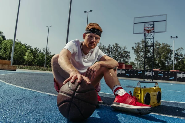 Basketball player in sportswear and bandana sitting on court with ball and tape recorder — Fotografia de Stock