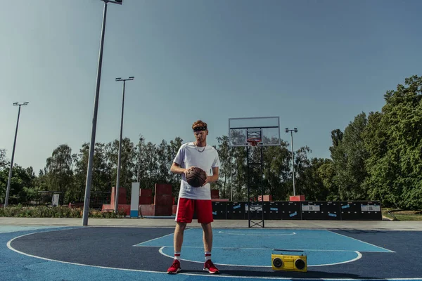 На всю длину баскетболиста в спортивной одежде, стоящего с мячом возле магнитофона — стоковое фото