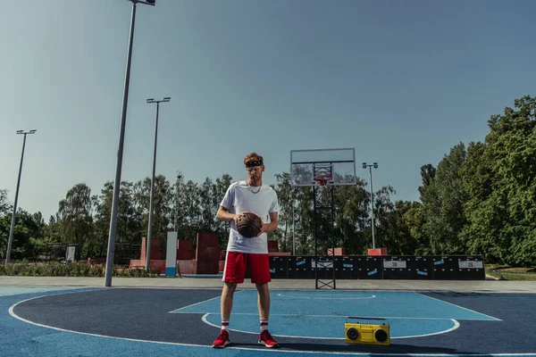 Full length of basketball player in sportswear standing with ball near tape recorder - foto de stock