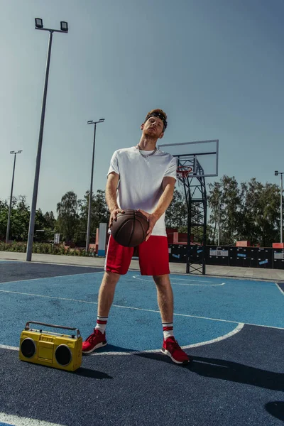 Full length of basketball player standing near boombox with ball — Stockfoto