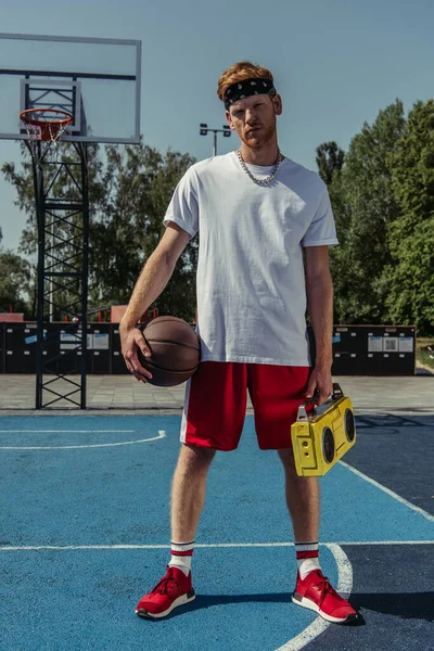 Молодой баскетболист с мячом и бумбоксом смотрит в камеру на корте — стоковое фото