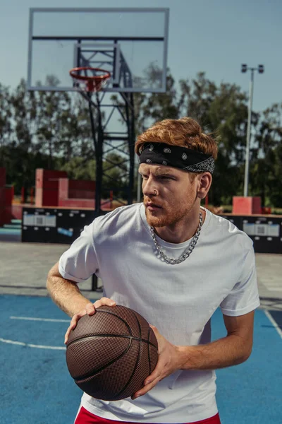 Young sportsman in bandana and necklace playing basketball outdoors — Stock Photo