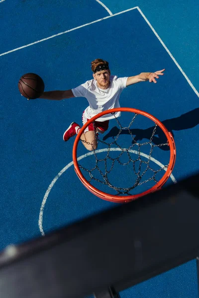 Top view of young sportsman jumping with ball under basketball ring — Foto stock