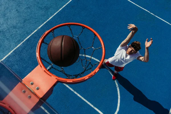 Top view of ball in basketball ring and young man training on court — Photo de stock