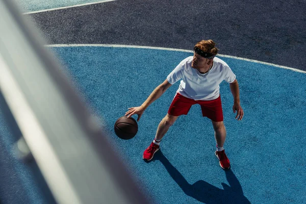 Высокий угол обзора спортивного человека, играющего в баскетбол на корте на размытом переднем плане — стоковое фото