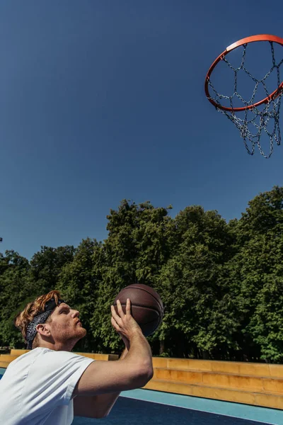 Side view of redhead man in bandana playing basketball outdoors — Fotografia de Stock