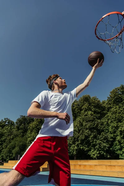 Low angle view of man in sportswear throwing ball into basketball hoop — Photo de stock