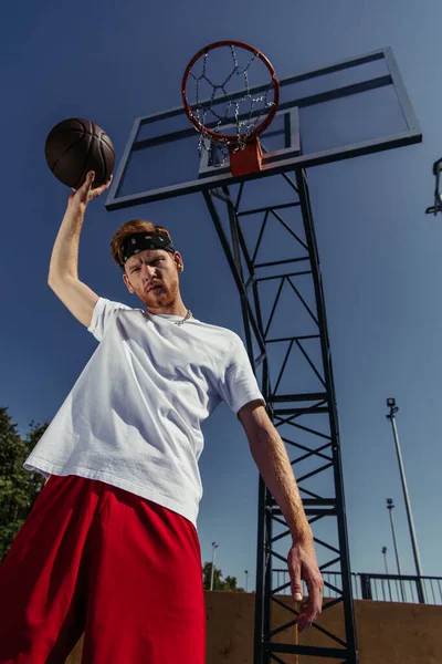 Low angle view of sportsman in white t-shirt standing under basketball ring — Photo de stock