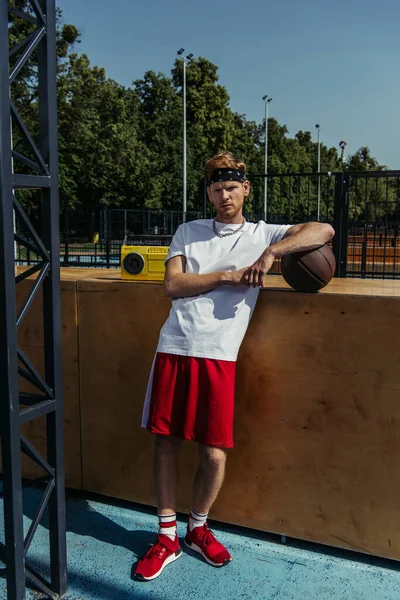 Full length of basketball player in red shorts standing near boombox and looking at camera - foto de stock