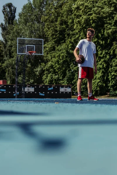 Full length of basketball player in sportswear standing with ball on modern court — Stock Photo