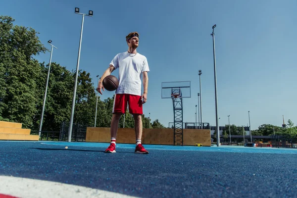 Full length of basketball player in sportswear standing with ball on modern court — Stockfoto