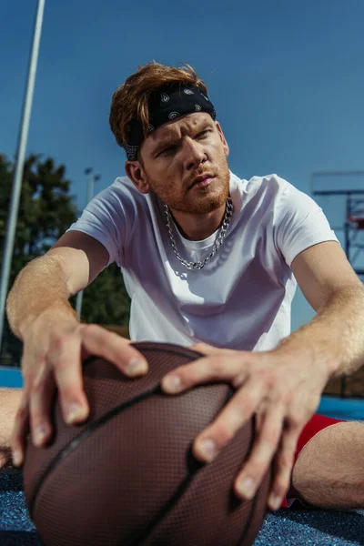 Sportive man in necklace and bandana looking away near blurred ball — Photo de stock