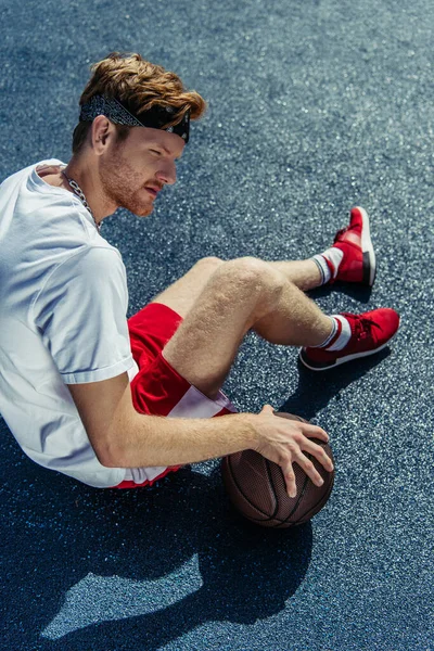 High angle view of man in sportswear sitting on stadium with ball - foto de stock