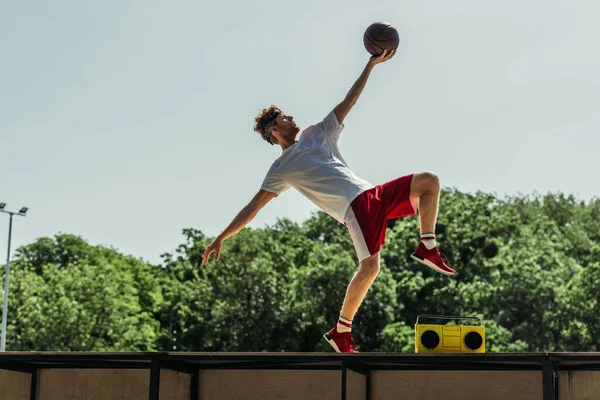 Side view of man in sportswear playing basketball near record player — Stock Photo