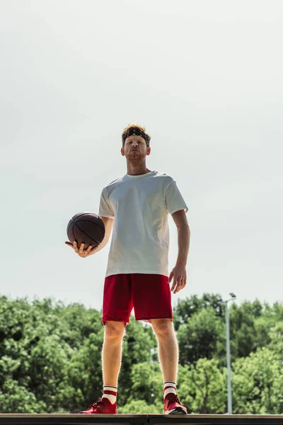 Full length of young basketball player in sportswear standing with ball outdoors — Stockfoto