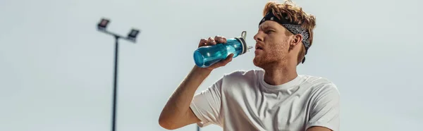 Young sportsman drinking refreshing water from sports bottle outdoors, banner — Photo de stock