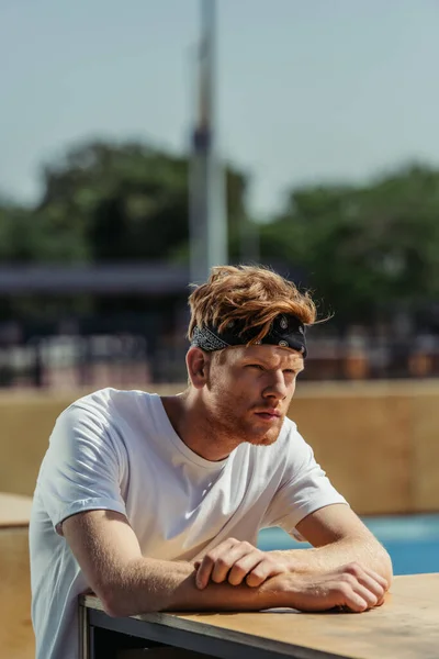Pensive redhead sportsman in white t-shirt and bandana looking away outdoors - foto de stock