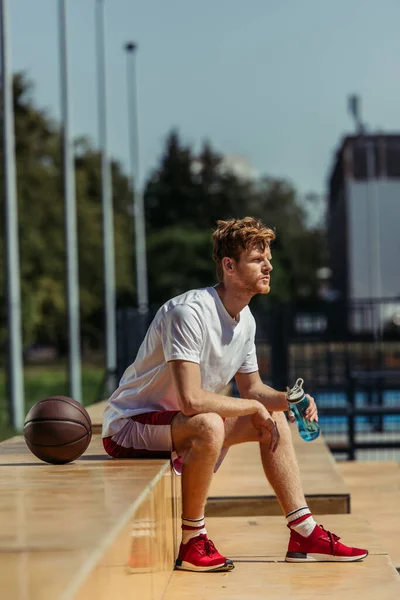 Full length of man in red sneakers sitting with sports bottle near ball — Fotografia de Stock