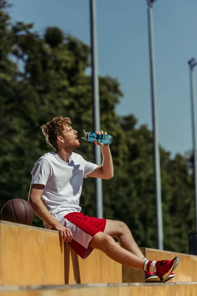 Thirsty sportsman sitting on stadium and drinking fresh water from sports bottle — Foto stock