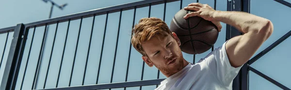 Low angle view of basketball player with ball standing near fence outdoors, banner - foto de stock