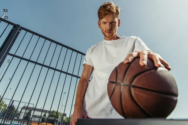 Low angle view of confident basketball player looking at camera near blurred ball — Photo de stock