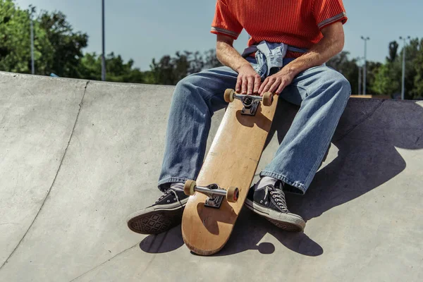 Обрезанный вид на фигуриста в джинсах, сидящего на рампе в скейт-парке — стоковое фото