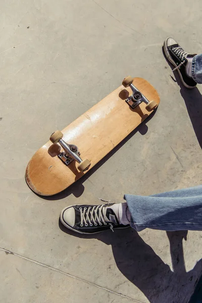 Cropped view of man in gumshoes near skateboard lying upside down — Stock Photo