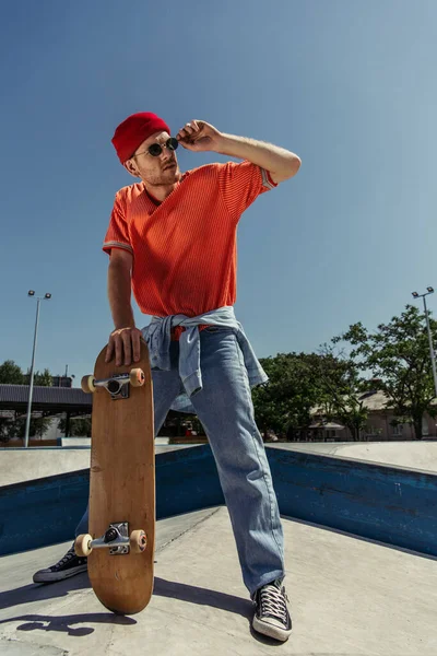 Full length of man adjusting trendy sunglasses while standing with skate in park — Stock Photo