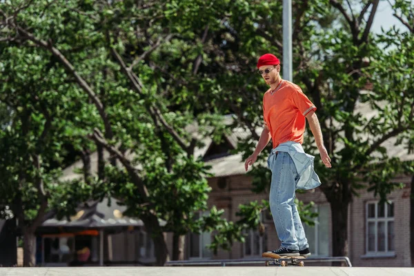 Full length of man in stylish outfit skateboarding in blurred city park — Stock Photo