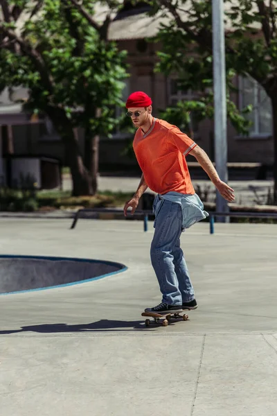 Full length of stylish skateboarder in sunglasses and beanie riding in city park — Stock Photo