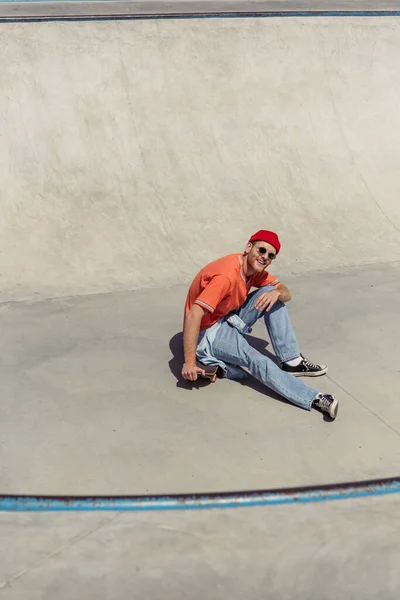 High angle view of smiling man in trendy clothes sitting on skate and looking at camera — Stockfoto