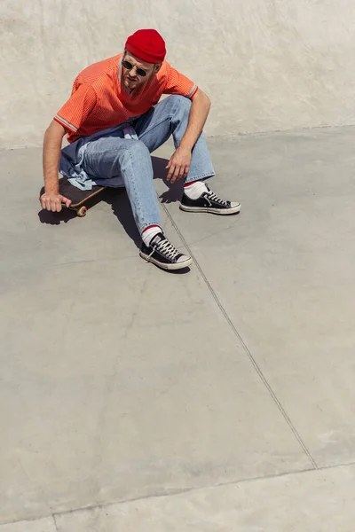 Young man in gumshoes sitting on skateboard in skate park - foto de stock