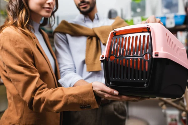 Cropped view of woman holding animal cage near blurred boyfriend in pet shop — Stock Photo