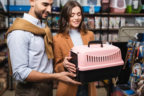 Smiling muslim man looking at animal cage near girlfriend in pet shop — Stock Photo