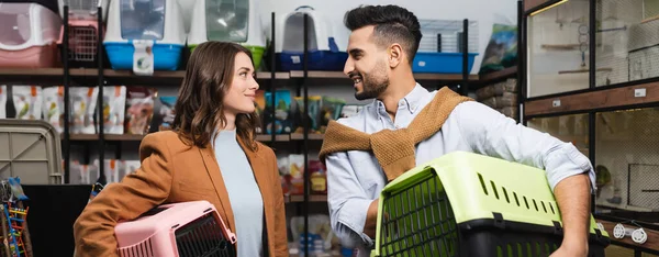 Positive interracial couple holding animal cages in pet shop, banner — Stock Photo