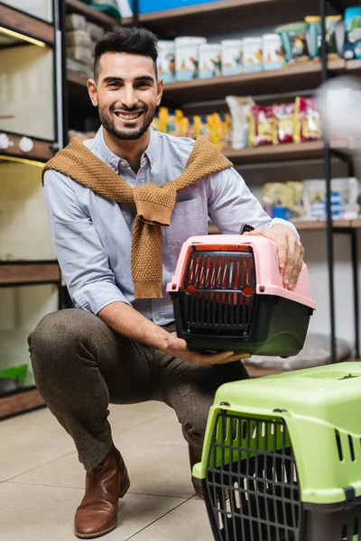 Cheerful arabian man holding pet cage and looking at camera in pet shop — Stock Photo