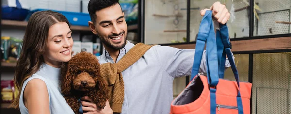 Muslim man holding animal dog near girlfriend with poodle in store, banner — Stock Photo