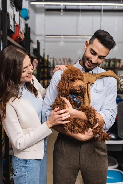 Smiling interracial couple holding poodle in pet shop — Foto stock