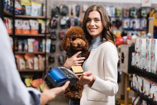 Smiling customer paying with credit card and holding poodle in pet shop — Stock Photo
