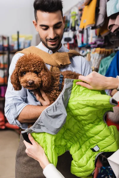 Woman holding animal jacket near arabian boyfriend with poodle in pet shop — Foto stock