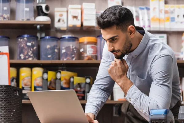 Muslim seller using laptop near payment terminal in pet shop — Stockfoto
