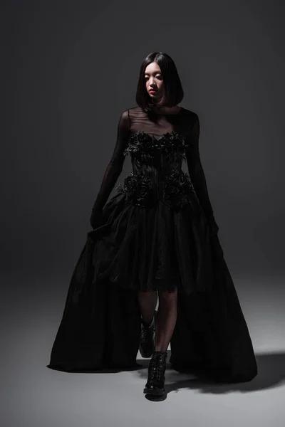 Full length of asian young woman in gothic dress and boots posing on dark grey — Stock Photo