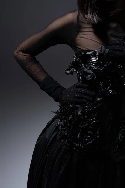 Cropped view of woman in black gothic dress and gloves posing with hand on hip on dark grey — Fotografia de Stock