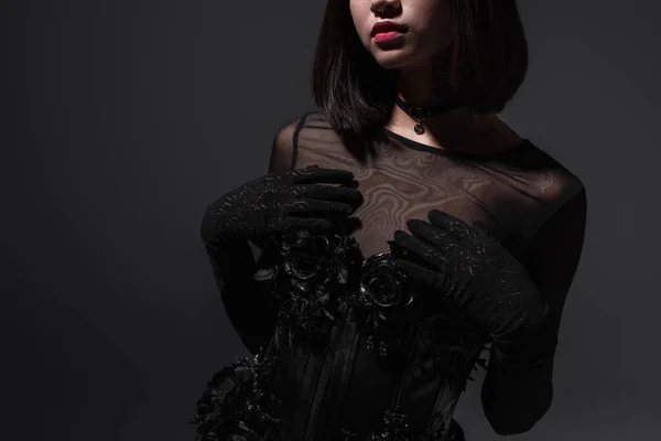 Cropped view of brunette young woman in black gothic dress and gloves posing on dark grey — Fotografia de Stock