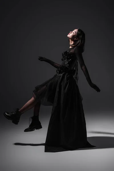 Side view of asian young woman in black gothic dress and boots levitating on dark grey — Photo de stock