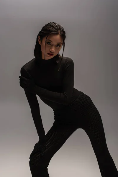 Pretty and young asian model in black outfit with gloves posing isolated on grey — Photo de stock