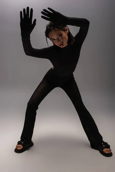 Full length of stylish asian woman in total black outfit gesturing while posing on grey — Photo de stock