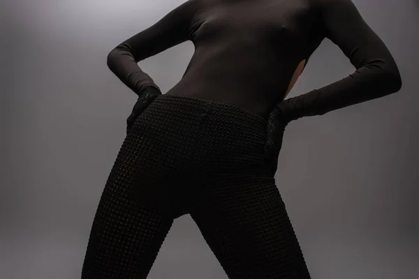 Cropped view of model in black outfit with gloves posing with hands on hips isolated on grey — Stock Photo
