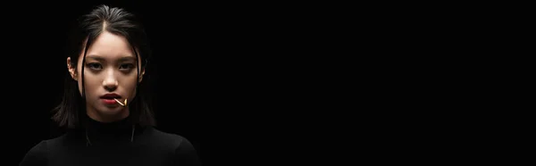 Portrait of pretty asian woman with burning matchstick in mouth looking at camera isolated on black, banner — Stock Photo