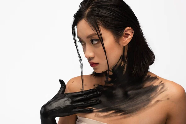 Young asian woman with naked shoulders and hand in black paint touching body isolated on white — Stock Photo